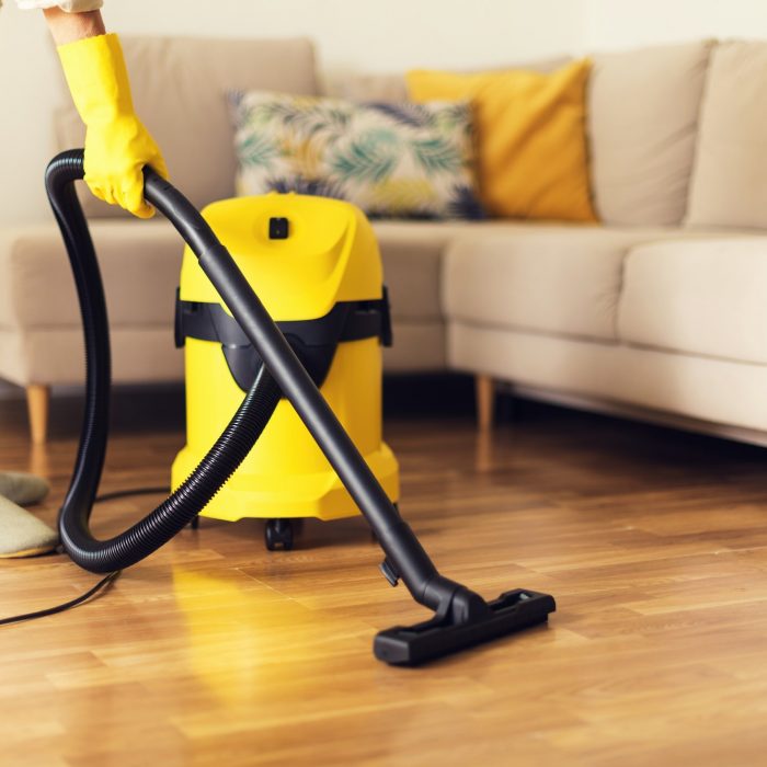 Woman cleaning sofa with yellow vacuum cleaner. Copy space. Cleaning service concept